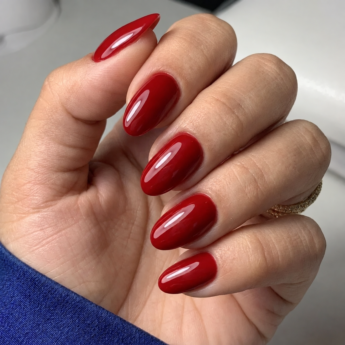 After Dark (Oval) glossy deep red press-on nails on a hand with a blue sleeve in soft natural light