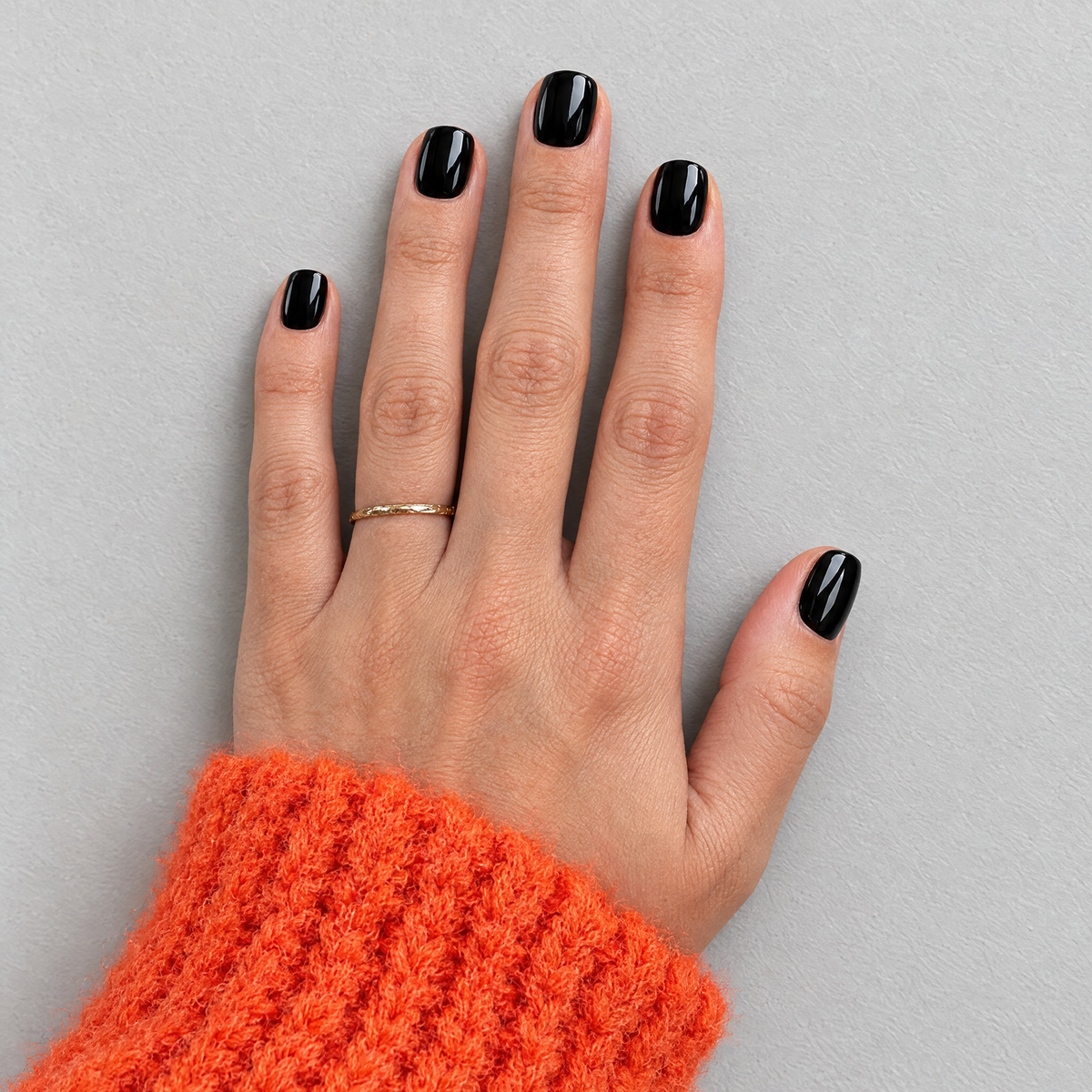 Black Tie (Extra-Short) glossy black press-on nails, overhead flat lay with orange knit sleeve